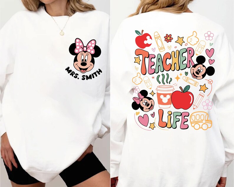 May include: White sweatshirt with a Minnie Mouse design, pink bow, and the name "Mrs. Smith" on the front. The back has the words "Teacher Life" with colourful graphics of apples, pencils, and Mickey Mouse.