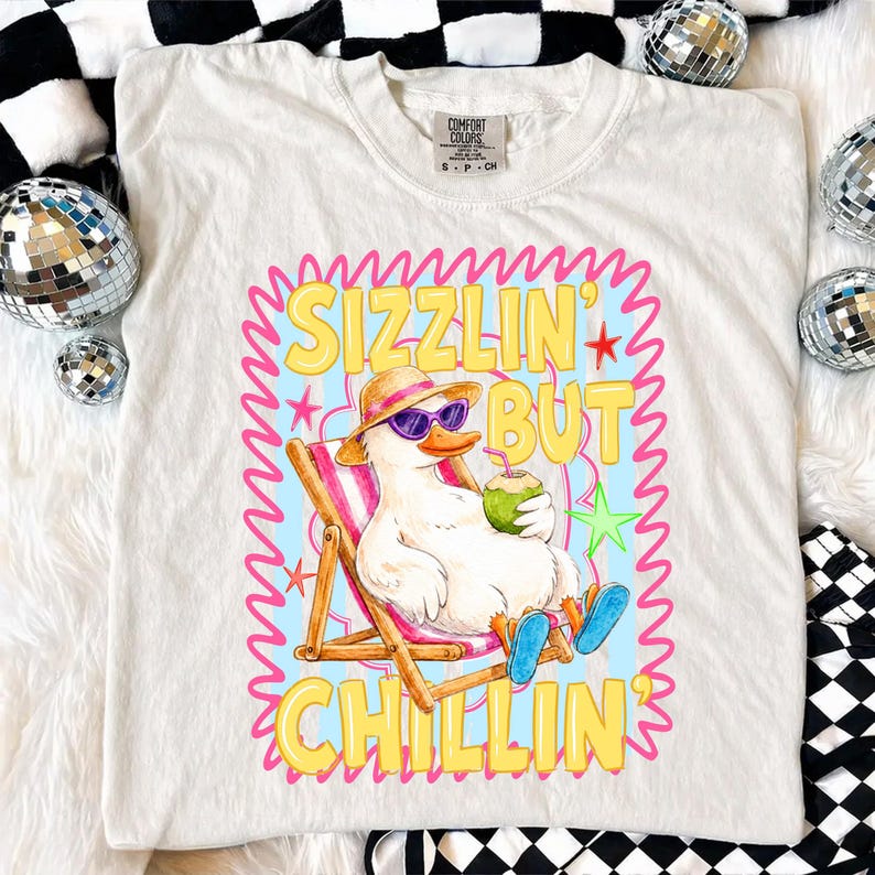 May include: White Comfort Colors t-shirt featuring a cartoon duck wearing sunglasses and a hat, relaxing in a beach chair and holding a coconut drink. The shirt has the text "Sizzlin' But Chillin'" in a colorful design.