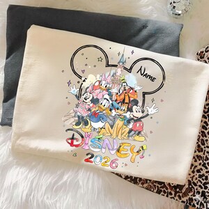 May include: A cream-colored pillowcase featuring a colorful Disney character design. The design includes Mickey Mouse, Minnie Mouse, Donald Duck, Goofy, and Daisy Duck, with the word "Disney" and the year "2026". The word "Name" is also visible.