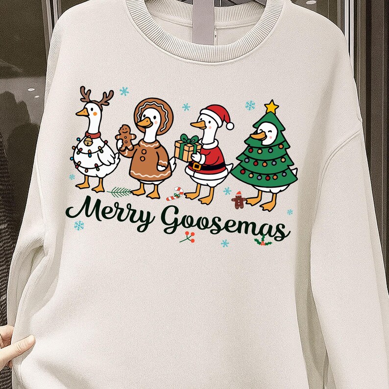 Peut inclure: Sweat-shirt cr&egrave;me avec un motif festif repr&eacute;sentant quatre oies de dessin anim&eacute; habill&eacute;es pour No&euml;l. Une oie porte des bois de renne, une autre tient un biscuit en pain d'&eacute;pices et une autre est habill&eacute;e en P&egrave;re No&euml;l. Le texte "Merry Goosemas" est &eacute;crit en dessous.