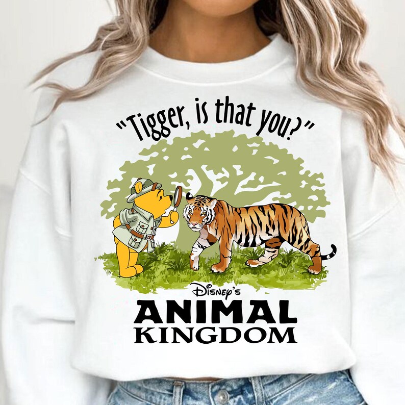 Puede incluir: Sudadera blanca con un gr&aacute;fico de Winnie de Pooh mirando a un tigre a trav&eacute;s de una lupa. El texto "Tigger, is that you?" est&aacute; por encima del gr&aacute;fico y "Disney's Animal Kingdom" est&aacute; por debajo del gr&aacute;fico.