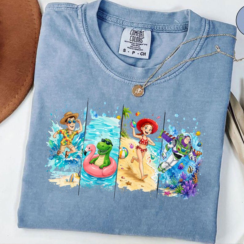 May include: A light blue Comfort Colors t-shirt featuring a colorful graphic of cartoon characters enjoying a beach vacation. The graphic includes a man in a Hawaiian shirt, a dinosaur in a flamingo float, a woman in a bikini, and Buzz Lightyear.