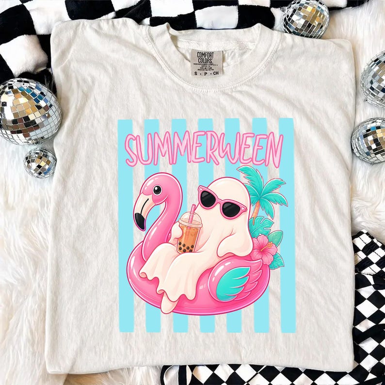 K&ouml;nnte beinhalten: Cremefarbenes T-Shirt mit einer Grafik eines Geistes mit Sonnenbrille, der auf einem rosa Flamingo-Schwimmring schwimmt. Der Geist h&auml;lt ein Getr&auml;nk. Das Wort "SUMMERWEEN" steht in rosa Buchstaben &uuml;ber der Grafik.