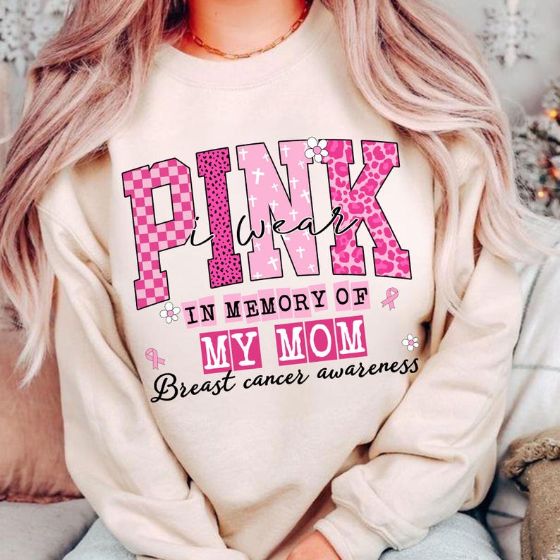 K&ouml;nnte beinhalten: Beiges Sweatshirt mit dem Schriftzug "PINK I wear" in rosa, gemusterten Buchstaben. Darunter steht "IN MEMORY OF MY MOM" und darunter "Breast cancer awareness". Rosa Schleifen und Blumen sind ebenfalls abgebildet.