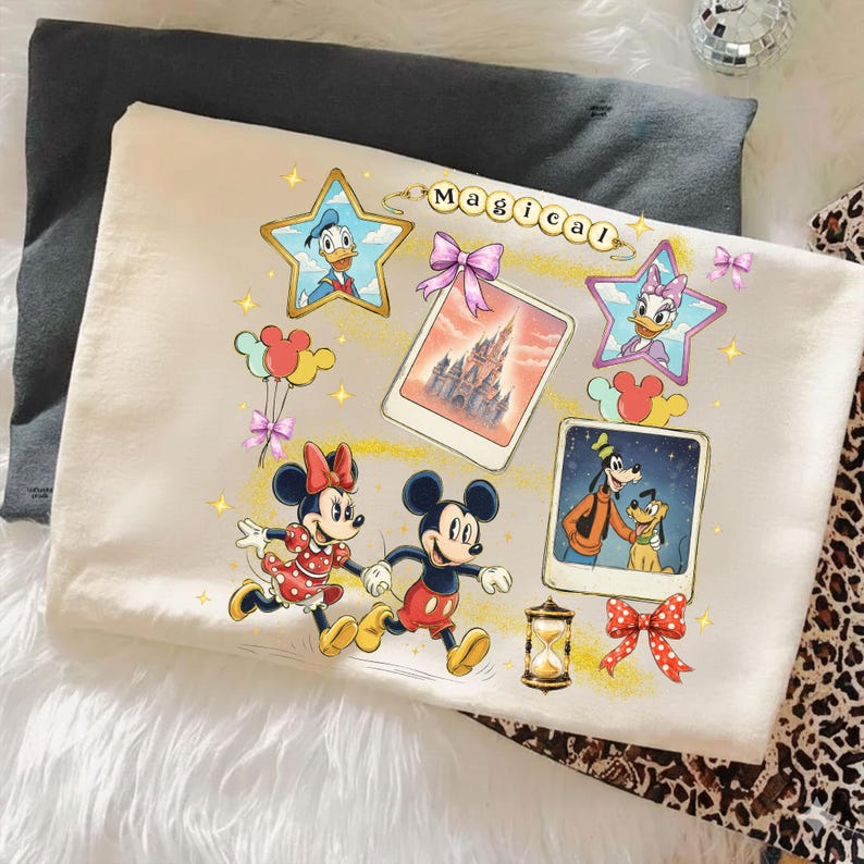 May include: Cream-colored t-shirt featuring Disney characters Mickey and Minnie Mouse, running. The shirt has a "Magical" design with Donald Duck, Daisy Duck, and Goofy. Includes a castle image and Mickey Mouse balloons.