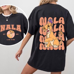 May include: Black t-shirt with a graphic of Nala from The Lion King. The graphic features Nala sitting with a butterfly on her head. The text "Nala" is repeated in a peach color around Nala.