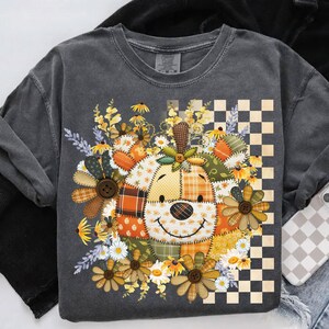 May include: Dark gray sweatshirt featuring a patchwork dog design with floral accents and a checkered pattern. The dog's face is made of various fabrics, with a smiling expression. The design includes daisies and button details.