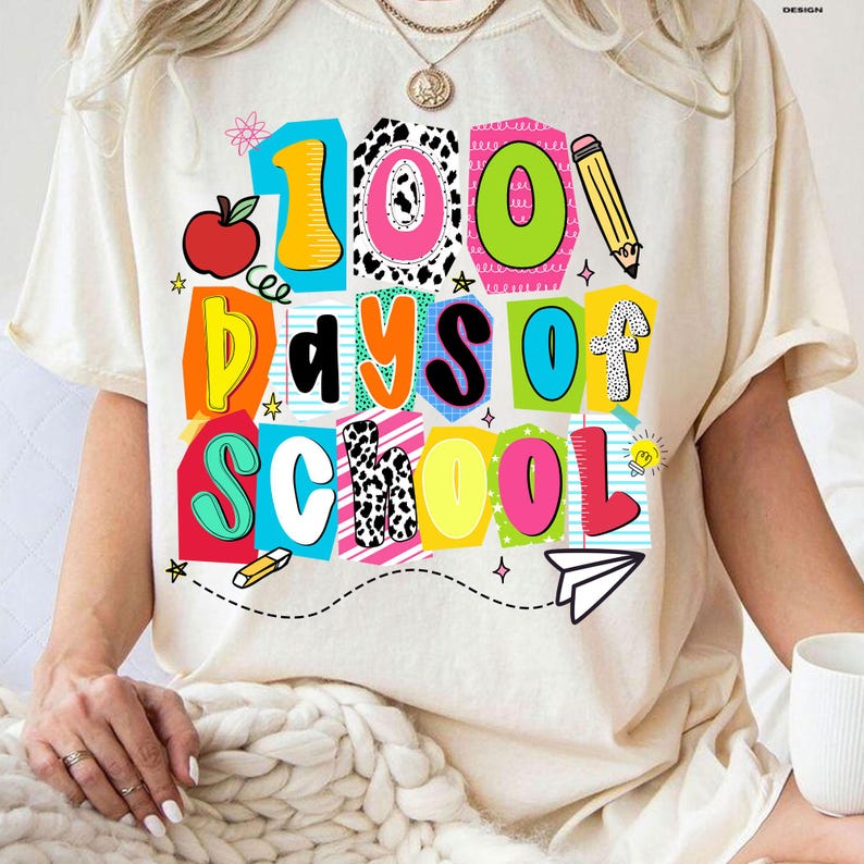 May include: Cream-colored t-shirt with a colorful graphic that reads "100 Days of School." The design includes a red apple, pencil, and paper airplane. The text is in various bright colors and fonts.