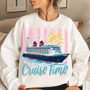 May include: White sweatshirt featuring a cruise ship illustration, pink stripes, and a yellow sun. The text "Cruise Time" is in blue and yellow. The sweatshirt is a casual style, suitable for leisure wear.