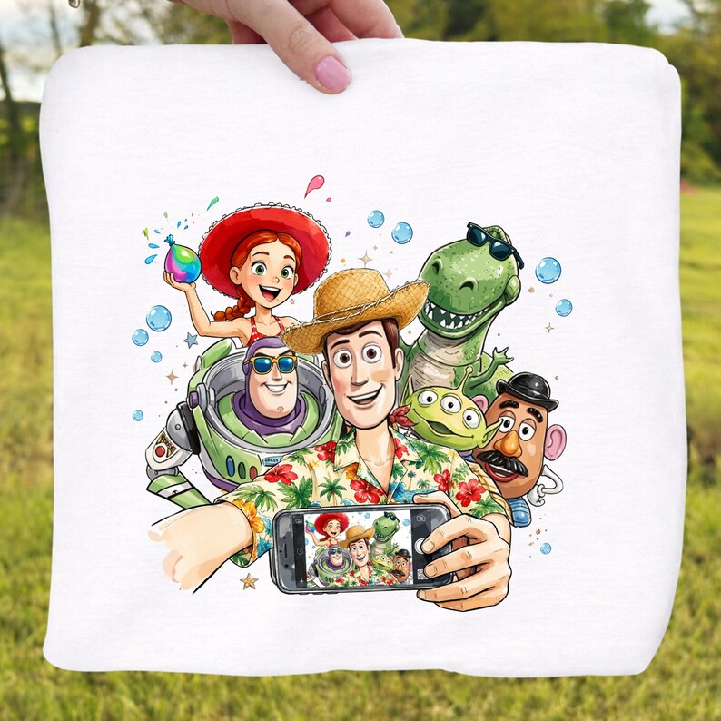May include: White square pillow featuring a colorful illustration of characters from the Toy Story movie taking a selfie. The characters include Woody, Buzz Lightyear, Rex, and others. The pillow is held by a person.