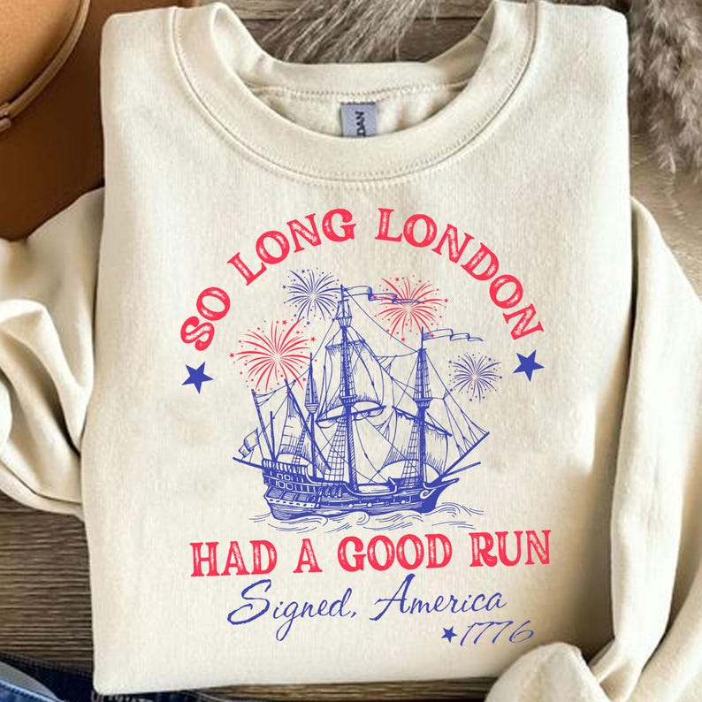 May include: Cream-colored sweatshirt with a graphic featuring a blue ship, fireworks, and text that reads "So Long London, Had a Good Run, Signed, America, *1776". The design includes red and blue accents.