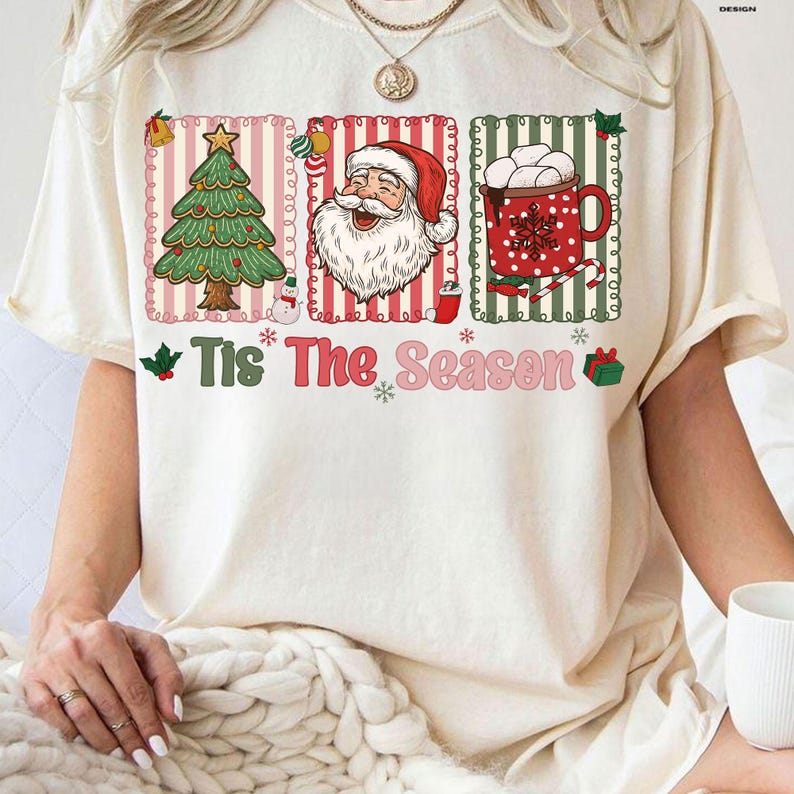 Puede incluir: Camiseta color crema con un dise&ntilde;o festivo. El dise&ntilde;o incluye un &aacute;rbol de Navidad, Pap&aacute; Noel y una taza de chocolate caliente, todo dentro de marcos rectangulares. La frase "Tis The Season" est&aacute; impresa debajo de las im&aacute;genes, con copos de nieve y una caja de regalo.