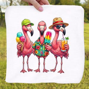 May include: A white towel featuring a whimsical illustration of three pink flamingos. One flamingo wears a green cap and holds an ice cream cone, another wears a Hawaiian shirt and holds a popsicle, and the third wears sunglasses and a straw hat, holding a drink.
