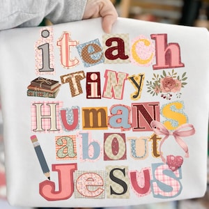 May include: White sweatshirt with the text "i teach tiny humans about Jesus" in a colorful, patchwork style. Features a pencil, books, flowers, and a bow.