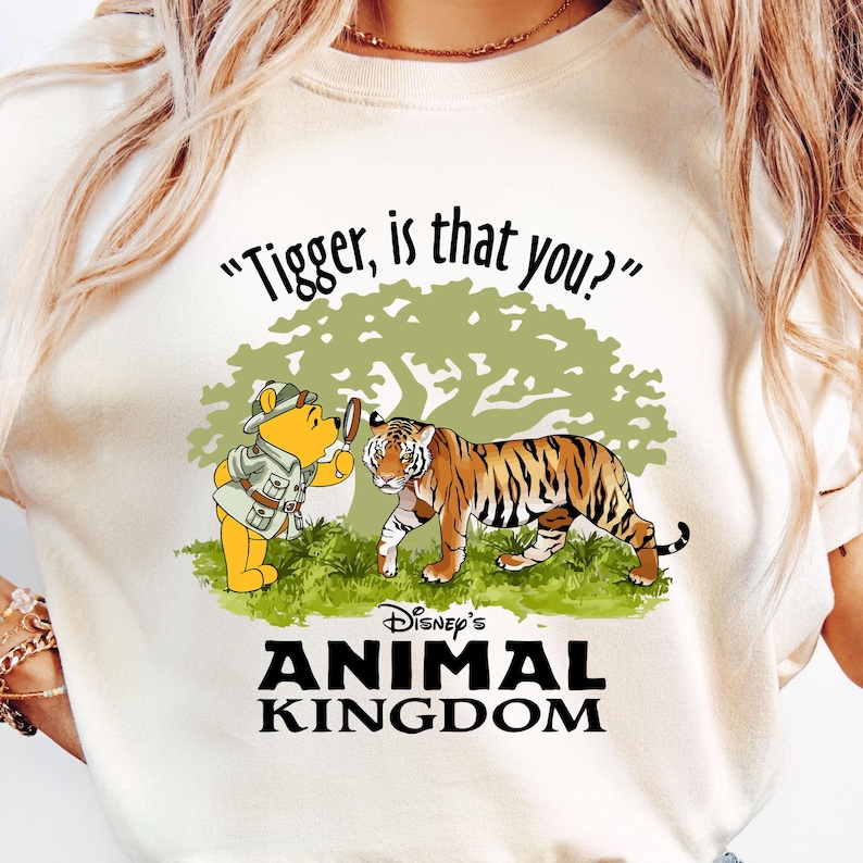 Puede incluir: Una camiseta blanca con una imagen de dibujos animados de Winnie de Pooh mirando a un tigre a trav&eacute;s de una lupa. El texto "Tigger, is that you?" est&aacute; por encima de la imagen. Debajo de la imagen est&aacute; el texto "Disney's Animal Kingdom".