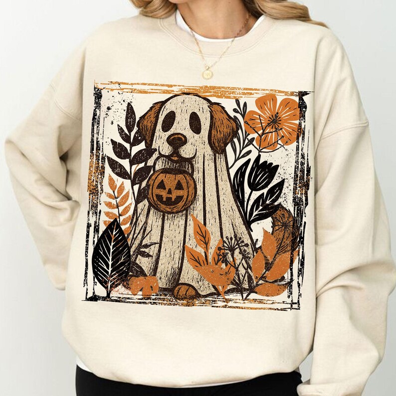 Pu&ograve; includere: Una felpa color crema con una grafica a tema Halloween. Il design presenta un cane vestito da fantasma che tiene in mano una zucca, circondato da foglie autunnali arancioni, nere e marroni. La grafica &egrave; incorniciata da un bordo nero.