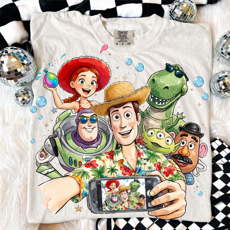 May include: White Comfort Colors t-shirt featuring a colorful graphic of Toy Story characters taking a selfie. Woody wears a straw hat and Hawaiian shirt. Other characters include Buzz Lightyear, Jessie, Rex, and Mr. Potato Head.