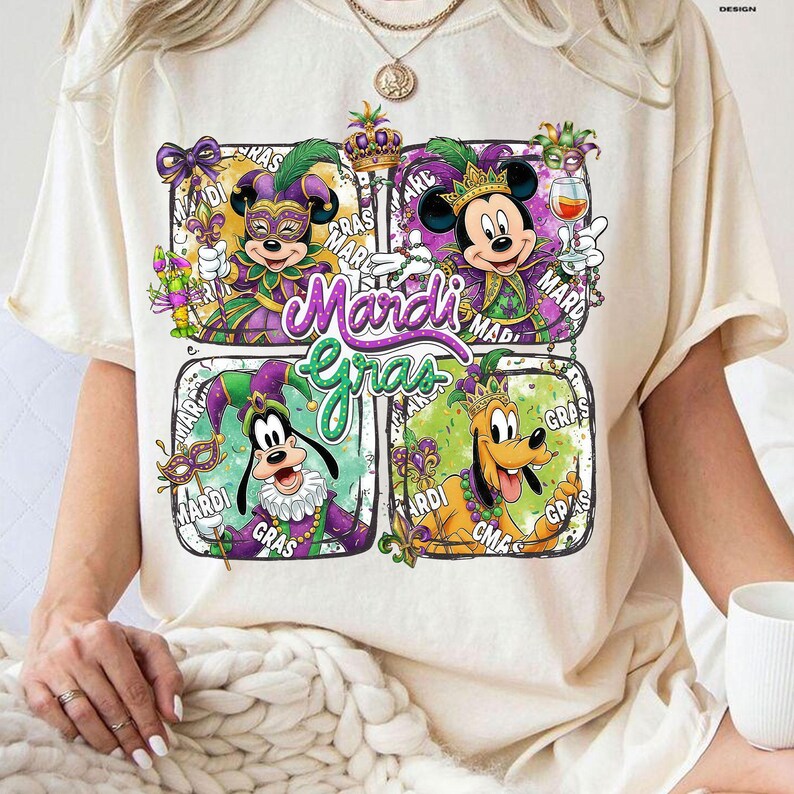 May include: Cream-colored t-shirt featuring a colorful Mardi Gras design. The graphic includes Mickey Mouse, Minnie Mouse, Goofy, and Pluto in festive attire, with the words "Mardi Gras" prominently displayed.