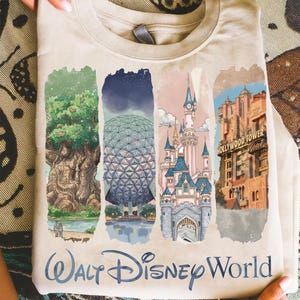 May include: A beige t-shirt featuring four colorful illustrations of Walt Disney World landmarks. The shirt includes images of the Tree of Life, Spaceship Earth, Cinderella Castle, and the Hollywood Tower Hotel. The words "Walt Disney World" are printed at the bottom.