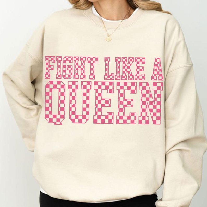 May include: A cream-colored sweatshirt with the text "FIGHT LIKE A QUEEN" in a pink checkered pattern. The sweatshirt has a crew neck and long sleeves, suitable for casual wear.