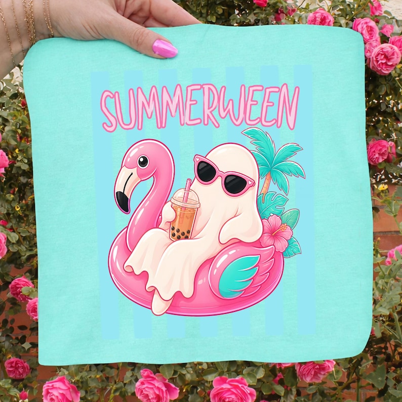 K&ouml;nnte beinhalten: Hellblaues Strandtuch mit dem Wort "SUMMERWEEN" in Rosa. Das Tuch zeigt einen Cartoon-Geist mit Sonnenbrille, der auf einem rosa Flamingo-Schwimmer treibt und Bubble Tea h&auml;lt. Palmen und Hibiskusbl&uuml;ten sind ebenfalls abgebildet.