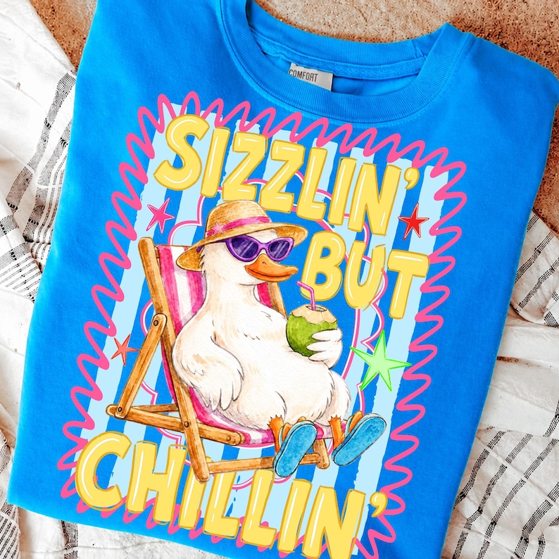 May include: A blue sweatshirt with a graphic of a duck wearing sunglasses and a hat, relaxing in a beach chair while holding a coconut drink. The text "Sizzlin' But Chillin'" is displayed in yellow.