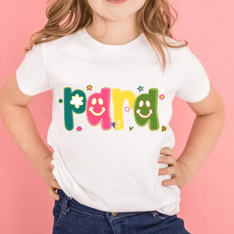 May include: White t-shirt with the word "para" in colorful, playful lettering. The letters are decorated with flowers, stars, and smiley faces. The shirt is worn by a child.