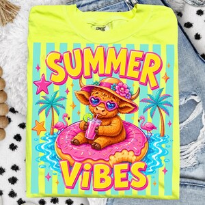 May include: Neon yellow t-shirt with a colorful graphic. The graphic features a cartoon Highland cow wearing heart-shaped sunglasses and a floral hat, floating on a pink donut in water. The words "SUMMER VIBES" are in large, bright letters.