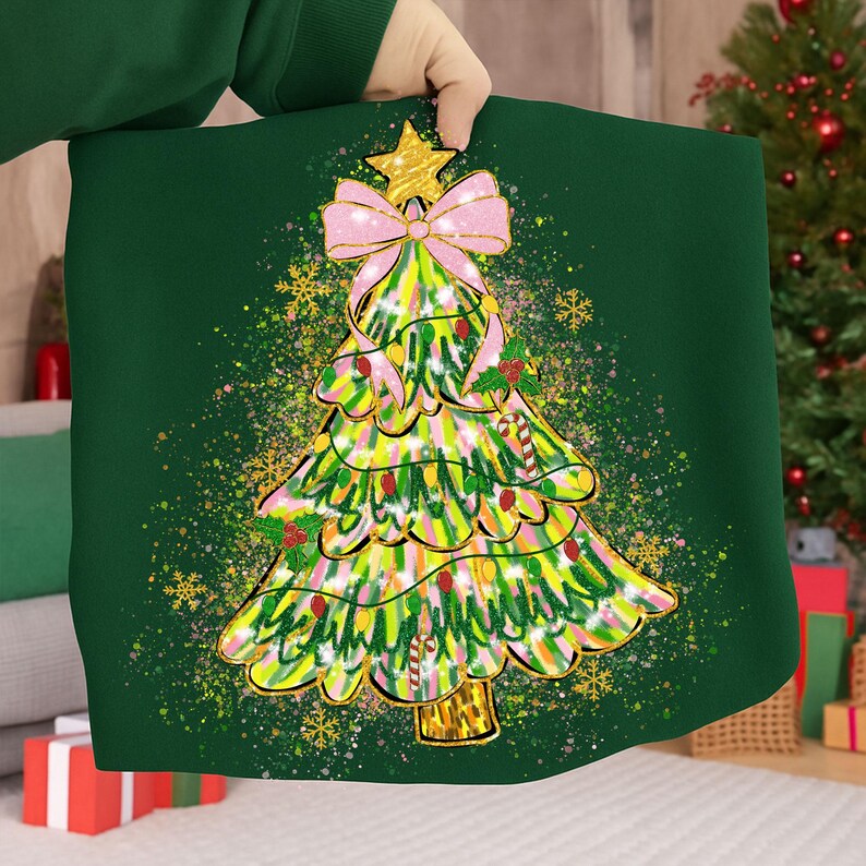 May include: A green Christmas-themed pillow with a colorful Christmas tree design. The tree features a pink bow, gold star, and candy cane accents. Gold snowflakes and glittery accents surround the tree, creating a festive holiday look.