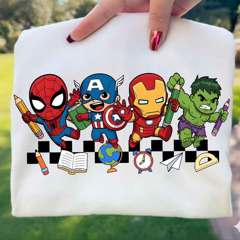 May include: A white sweatshirt featuring a colorful graphic of cartoon superheroes, including Spider-Man, Captain America, Iron Man, and the Hulk, each holding a pencil. Additional school-themed icons like a globe, book, and clock are also present.