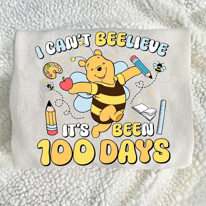 May include: A light gray sweatshirt with a colorful graphic featuring Winnie the Pooh as a bee, holding an apple and pencil. The text reads "I CAN'T BEELEIVE IT'S BEEN 100 DAYS" in yellow and blue.