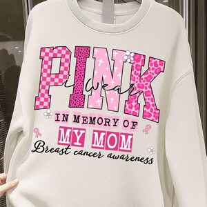 K&ouml;nnte beinhalten: Cremefarbenes Sweatshirt mit dem Schriftzug "PINK I WEAR" in Rosa, mit verschiedenen Mustern und einem floralen Akzent. Darunter steht "IN MEMORY OF MY MOM" und "Breast cancer awareness."