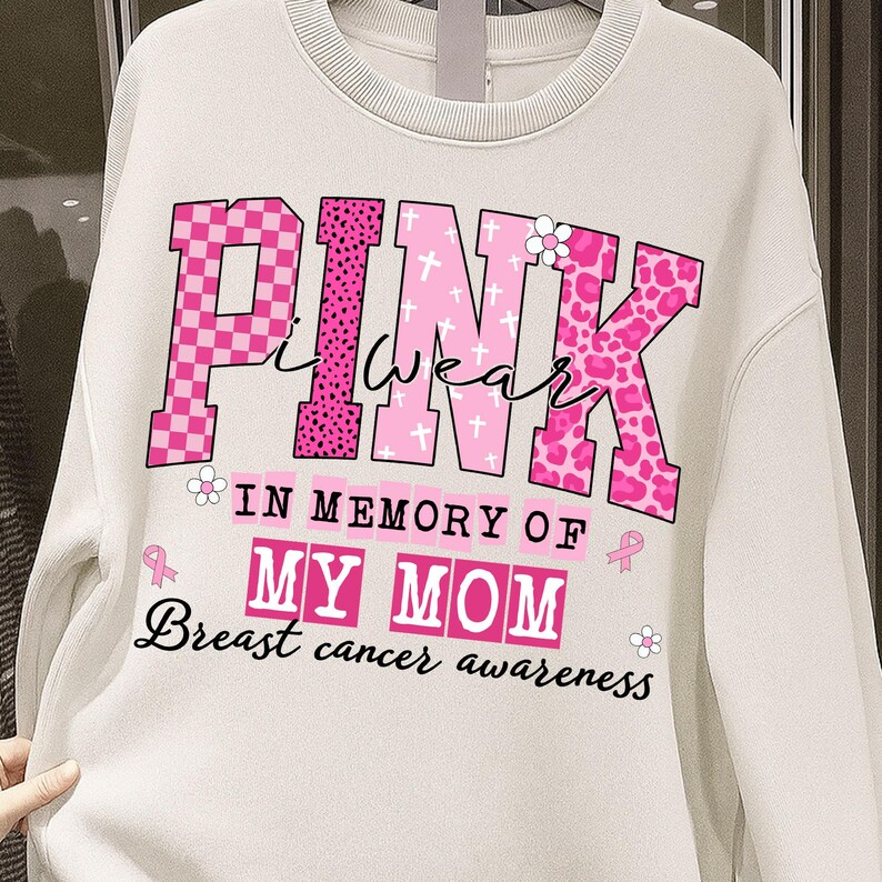 K&ouml;nnte beinhalten: Cremefarbenes Sweatshirt mit dem Schriftzug "PINK I WEAR" in Rosa, mit verschiedenen Mustern und einem floralen Akzent. Darunter steht "IN MEMORY OF MY MOM" und "Breast cancer awareness."