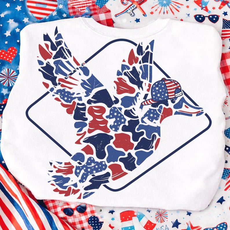 May include: White sweatshirt featuring a patriotic duck design. The duck is depicted with red, white, and blue camouflage-style patterns and a baseball cap. The design is enclosed within a dark blue diamond shape, perfect for celebrating Independence Day.
