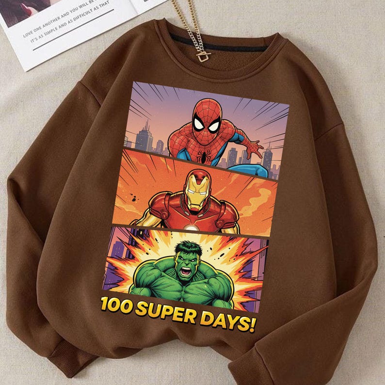 May include: Brown sweatshirt featuring a comic-style graphic of Spider-Man, Iron Man, and the Hulk. The graphic is divided into three panels with a cityscape background. Text at the bottom reads "100 SUPER DAYS!"