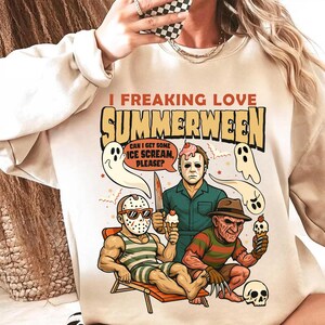 May include: Beige crewneck sweatshirt with a graphic that reads "I Freaking Love Summerween." The graphic features horror movie characters holding ice cream cones, with ghosts and a skull. The design is in shades of brown, red, and white.