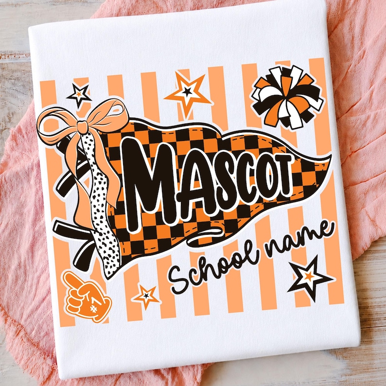 May include: A white t-shirt featuring a graphic print of an orange and black checkered pennant with the text MASCOT and School name. The design includes a bow, a pom-pom, a foam finger, and stars against a background of vertical orange stripes.