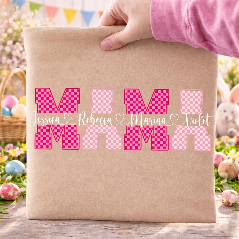May include: A beige tote bag with the word "MOM" in a pink checkered design. The names Jessica, Rebecca, Marina, and Violet are written below the letters. The bag is held by a person wearing a pink shirt.