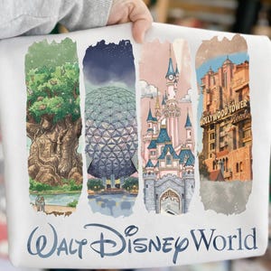 May include: White sweatshirt featuring watercolor illustrations of Disney World landmarks: the Tree of Life, Spaceship Earth, Cinderella Castle, and the Hollywood Tower Hotel. The words "Walt Disney World" are printed in blue script below the images.