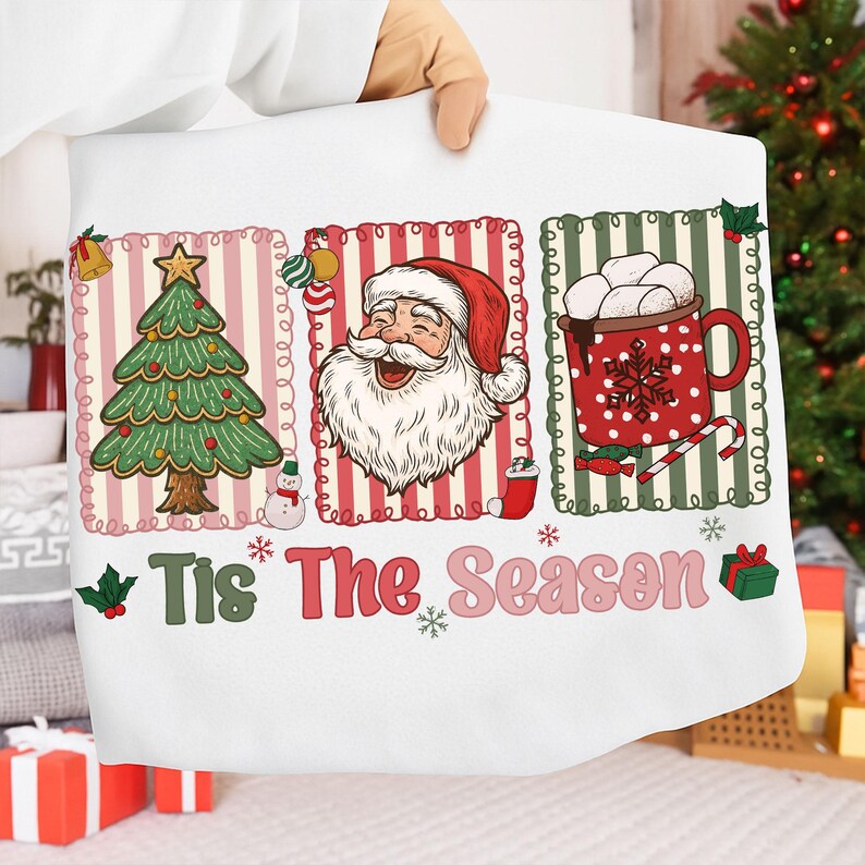Puede incluir: Funda de almohada blanca con tem&aacute;tica navide&ntilde;a con tres paneles ilustrados. Los paneles presentan un &aacute;rbol de Navidad, Pap&aacute; Noel y una taza de chocolate caliente. El texto "Tis The Season" se muestra en el centro.