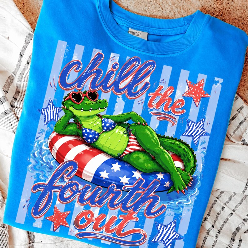 May include: A blue sweatshirt with a graphic of an alligator wearing sunglasses and a bikini, lounging on a patriotic float. The text "Chill the Fourth Out" is displayed in red and blue. Red and white stars are also featured.