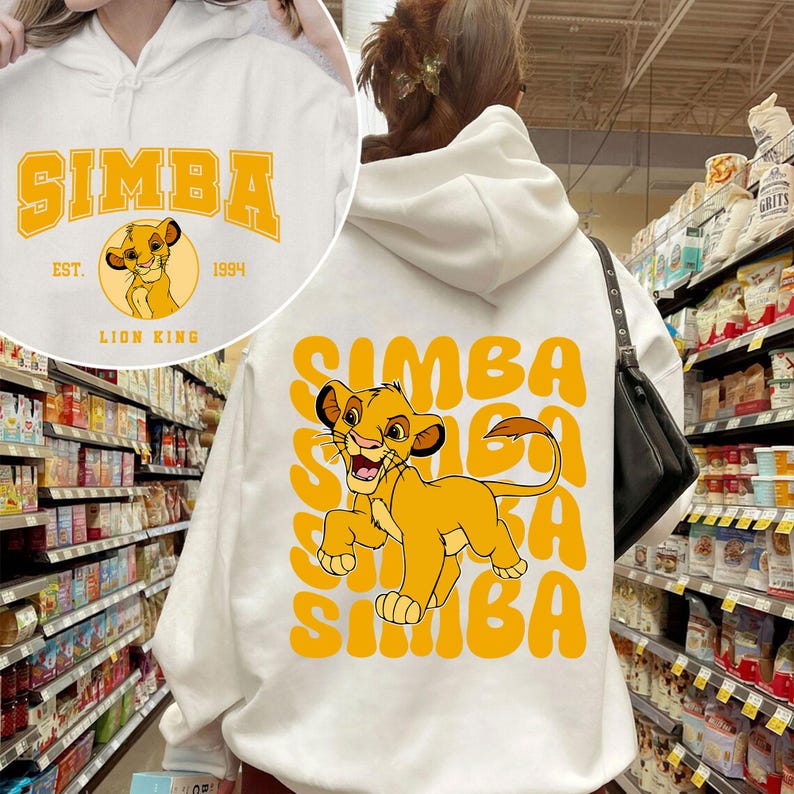 May include: White hooded sweatshirt with a graphic of Simba from The Lion King. The graphic features Simba in a yellow and orange color scheme with the text "SIMBA" in a yellow and orange color scheme.