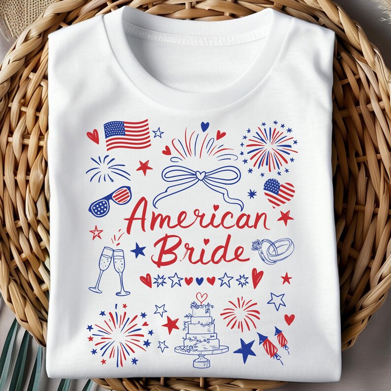 May include: White t-shirt with a patriotic design featuring the text "American Bride" in red script. The design includes an American flag, fireworks, hearts, stars, champagne glasses, and a wedding cake, all in red and blue.