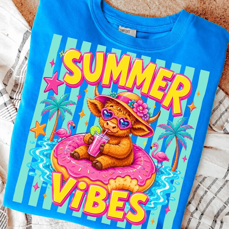 May include: A blue t-shirt with a colorful graphic. The graphic features a cartoon Highland cow wearing sunglasses and a hat, floating on a pink donut in water. The words "SUMMER VIBES" are written in yellow and pink.