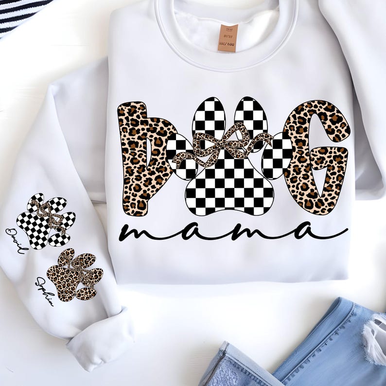 May include: White sweatshirt with "DOG mama" text in black script. The word "DOG" is designed with a leopard print and a checkered paw print. The sleeves feature paw prints with names.