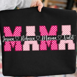 May include: Black sweatshirt with the word "MAMA" in pink checkered letters. Below the word "MAMA" are the names Jessica, Rebecca, Mariaa, and Violet in white script font, each separated by a heart symbol.