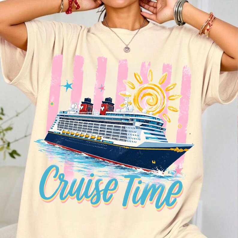 May include: Cream-coloured t-shirt featuring a cruise ship illustration with a sun and the text "Cruise Time" in blue. The ship is navy blue with red accents, set against pink vertical stripes and a blue ocean.
