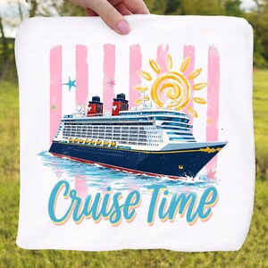 May include: White towel with a cruise ship illustration and the text "Cruise Time." The ship is navy blue with red accents, set against pink stripes and a yellow sun. The design includes blue water and stars.