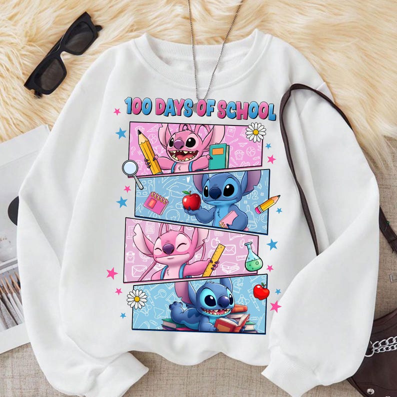 May include: White sweatshirt with a graphic of Stitch and Angel, and the text "100 Days of School". The design includes pencils, books, and apples. The sweatshirt has a crew neck and long sleeves. The design is in pink and blue.
