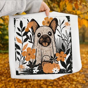 Pu&ograve; includere: Borsa tote bianca con un bulldog francese vestito da fantasma, circondato da fiori arancioni e foglie nere. Una zucca con manico &egrave; in basso. Il design ha un aspetto vintage, leggermente usurato.